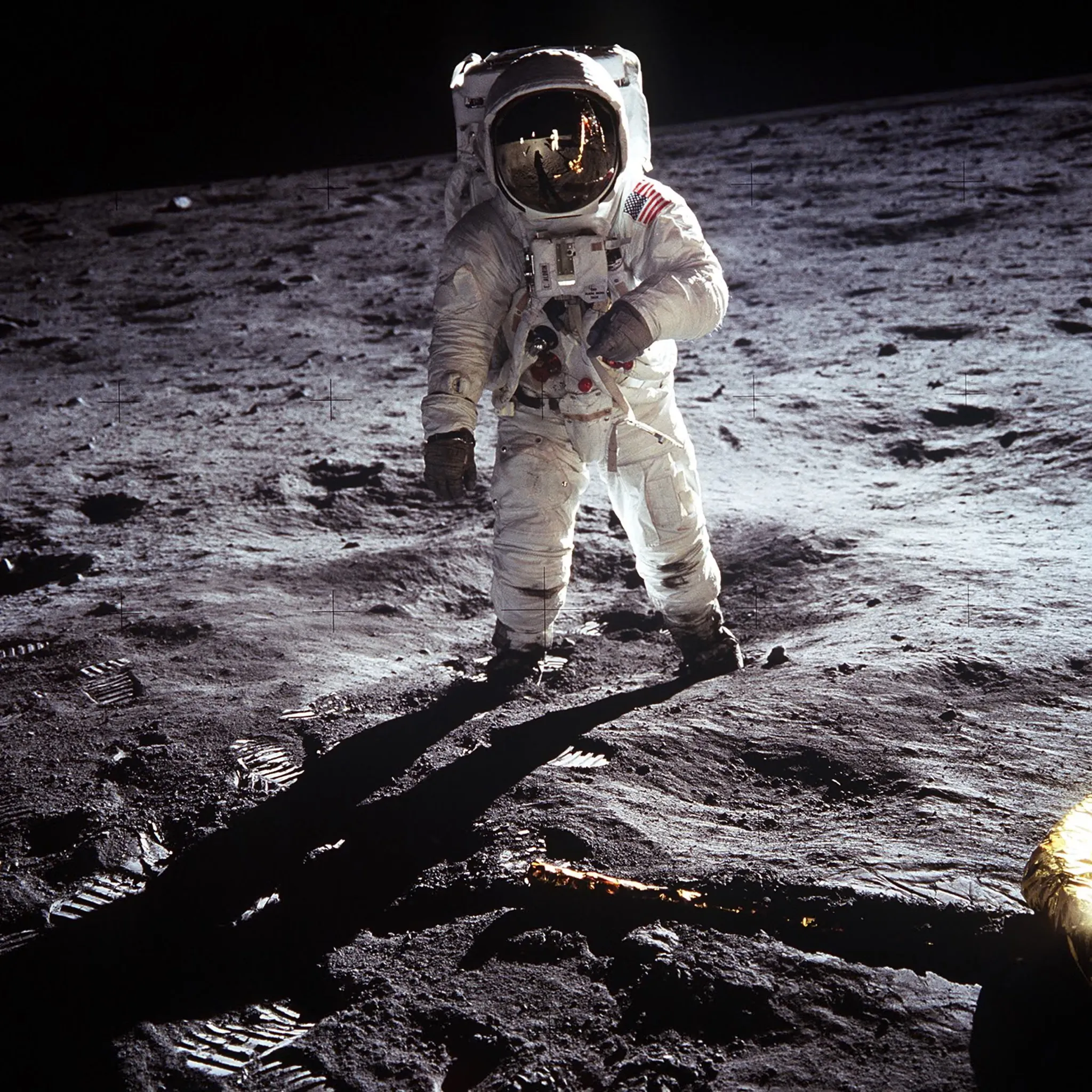 Buzz Aldrin standing on the Moon, with Neil Armstrong and the lunar module reflected in his gold visor