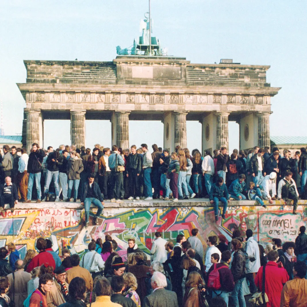 Crowds standing on the graffiti-covered Berlin Wall in front of the Brandenburg Gate, the day after the border opened