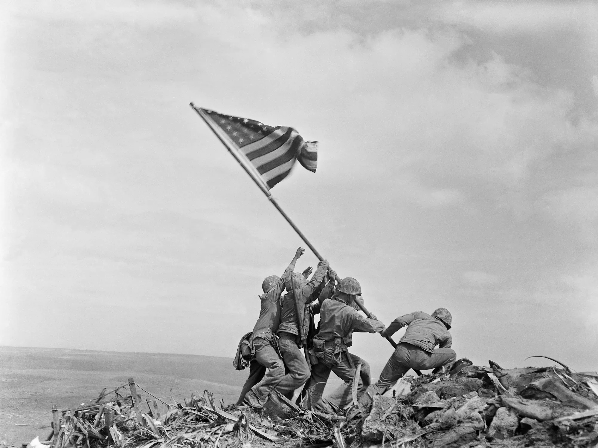 Six US Marines raising the American flag on a long pole atop Mount Suribachi during the Battle of Iwo Jima